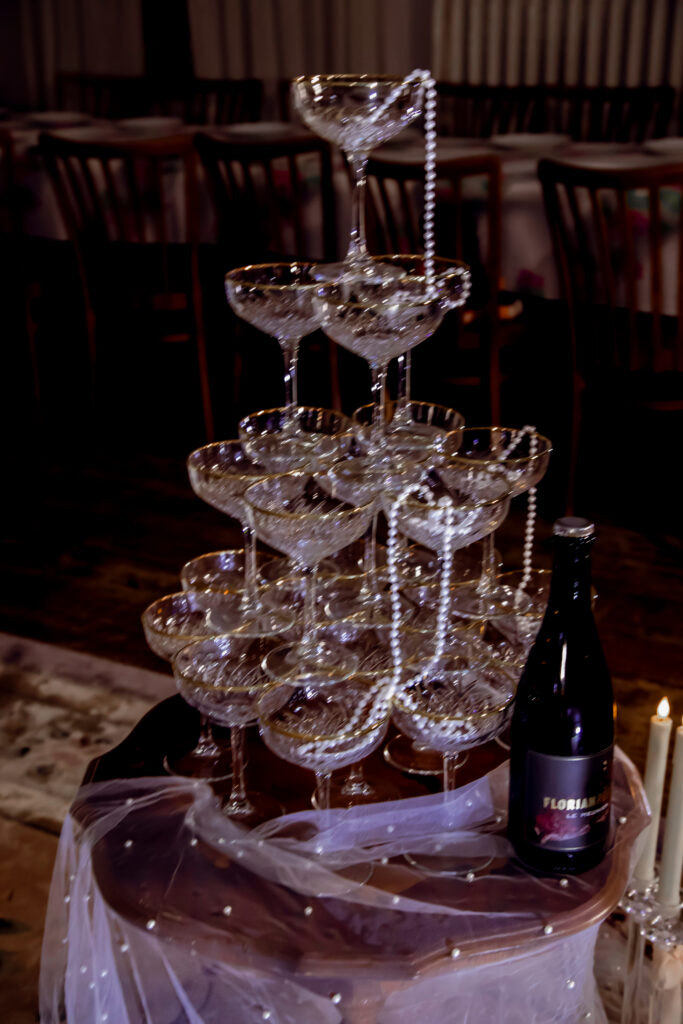 Diese elegante Sektpyramide, aufgenommen während einer Hochzeit im Schwarzwald bei Sand, stellt ein festliches Highlight der Feier dar. Der professionelle Hochzeitsfotograf aus Karlsruhe hat diese besondere Szene eingefangen, die die einzigartige Atmosphäre der Schwarzwaldhochzeit perfekt widerspiegelt. Die Sektpyramide, umgeben von stilvoller Hochzeitsdekoration, strahlt Glanz und Eleganz aus und trägt zu der romantischen Stimmung des Tages bei. Diese Detailaufnahme vermittelt das Gefühl einer unvergesslichen Hochzeit im Grünen, die durch die sorgfältig gewählte Dekoration und die besondere Pyramide bereichert wird.