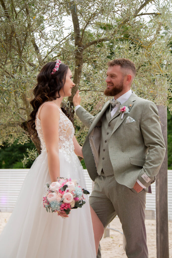 Dieses elegante Brautpaarshooting fand unter einem malerischen Olivenbaum im Sand bei einer traumhaften Hochzeit im Hubraum Durlach statt. Die Aufnahmen wurden von einem erfahrenen Hochzeitsfotografen aus Karlsruhe Durlach gemacht. Die Braut trägt ein zauberhaftes Brautkleid von Brautzauber, das ihre natürliche Schönheit perfekt zur Geltung bringt. Der Bräutigam zeigt sich in stilvoller Herrenmode von Style Bräutigamausstatter, die ihm einen modernen und eleganten Look verleiht. Die Kulisse des Olivenbaums und des Sandbodens schafft eine einzigartige Atmosphäre, die die Liebe des Brautpaares in all ihren Facetten widerspiegelt.